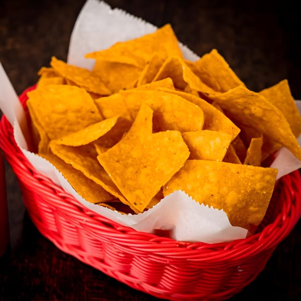 A red basket filled with crispy, golden tortilla chips, lined with white paper.